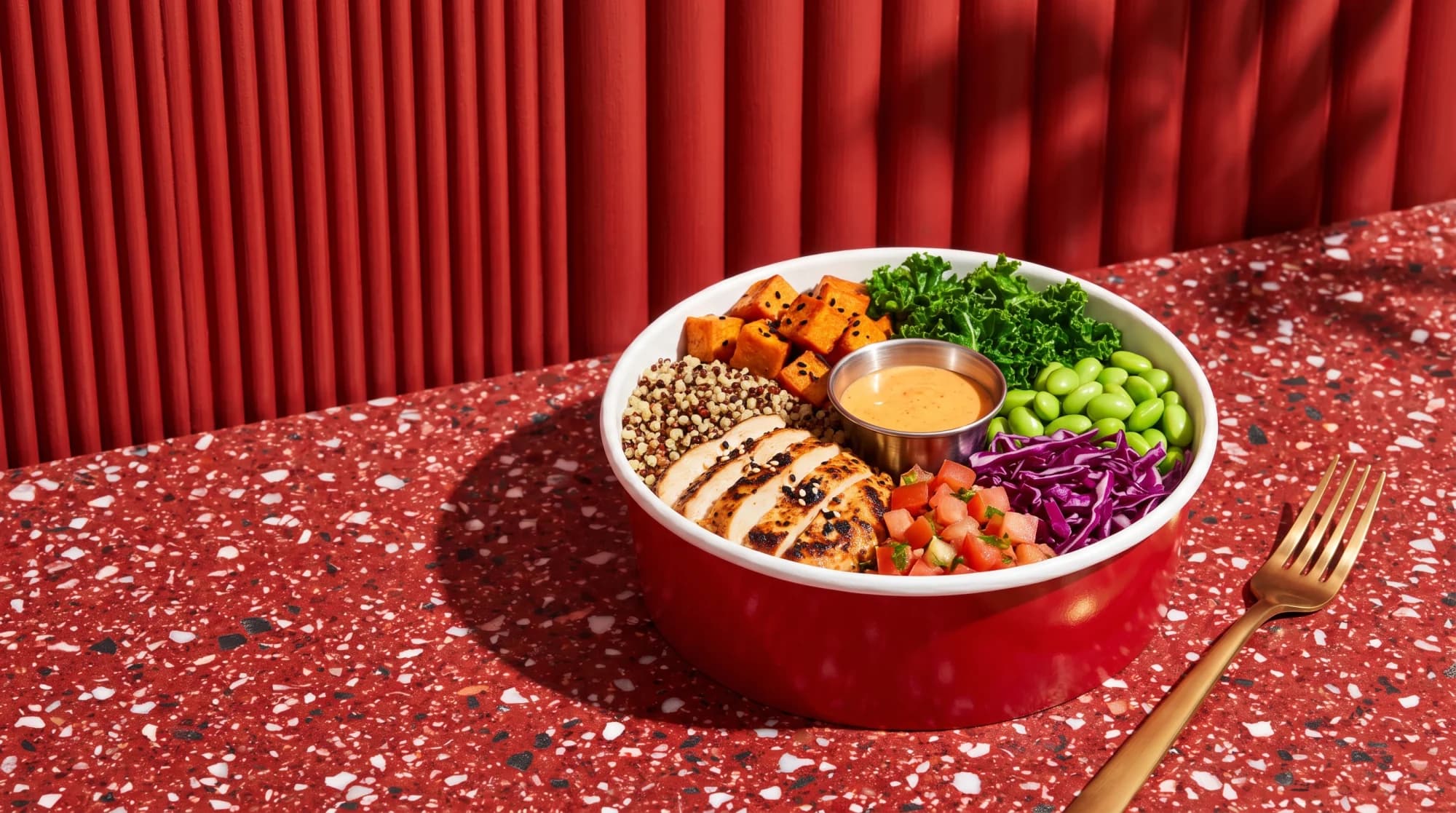 A Le Supreme bowl of grilled chicken, quinoa, sweet potato, kale and edamame on a red terrazzo counter